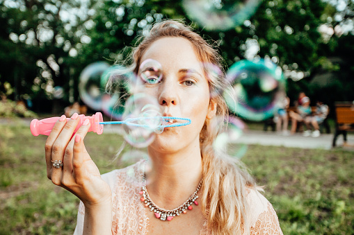 Beautiful bright portrait of romantic young girl inflating colorful soap bubbles in spring park