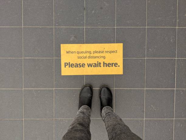 istock A pair of feet queuing at a 'Please wait here' sticker 1250417659