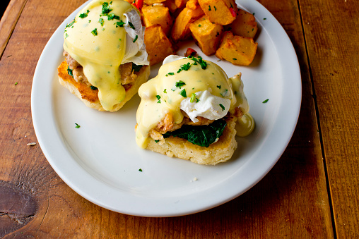 Eggs Benedict. Poached eggs w/ potato hash served in a cast iron skillet. English muffin. eggs, country ham, melted cheese, & homemade hollandaise sauce. Classic French or American cuisine favorite.