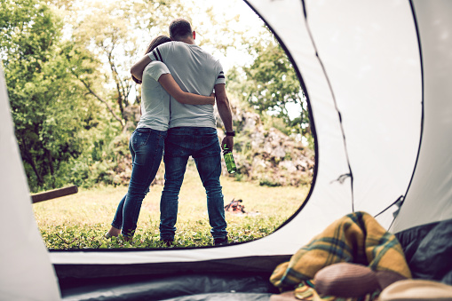 Couple Enjoying Beer And Embracing While Camping In Forest