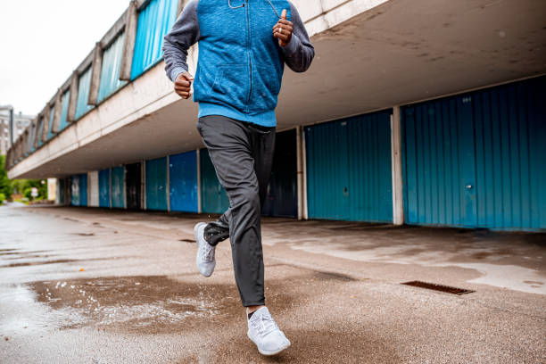 Young man running over the puddle by the garages Low section of a young african-american male athlete running over the puddle next to blue garages. jogging pants stock pictures, royalty-free photos & images