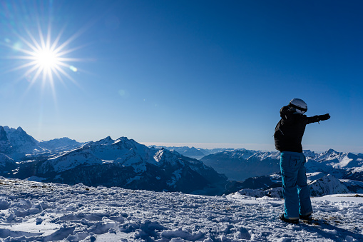 Girl enjoying sunbeams in winter with open arms at top of the mountain range. Snowboarder in late afternoon in the Swiss alps in winter. Spectacular view, for concept.
