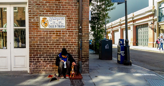 New Orleans, USA - Dec 10, 2017: A sunny day at the corner along Toulouse Street in the French Quarters. A homeless man feeds his companion dog.
