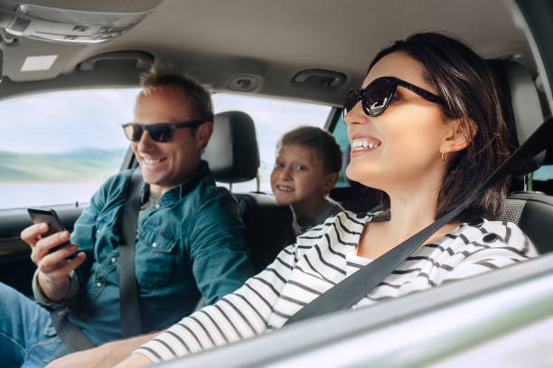 szczęśliwa rodzina auto podróży obraz koncepcyjny. widok wnętrza samochodu kobiety jazdy, człowiek do czynienia telefon komórkowy i mały synek uśmiecha się do kamery - fun mother sunglasses family zdjęcia i obrazy z banku zdjęć