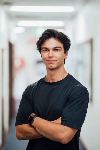 Male Student A close-up portrait of a young, Caucasian man looking at the camera smiling with his arms crossed. university students australia stock pictures, royalty-free photos & images