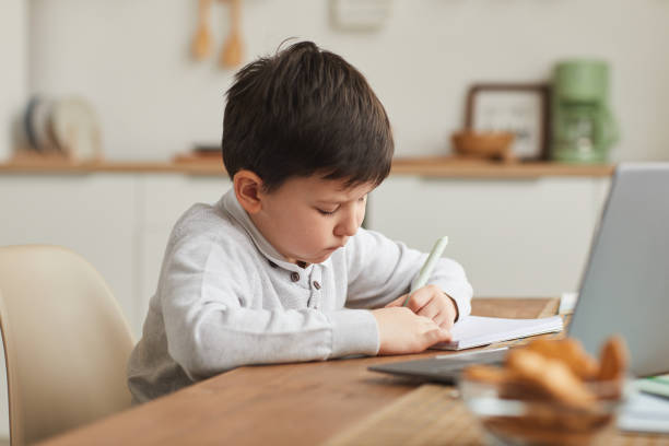istock Cute Little Boy Writing in Notebook at Home 1250438514