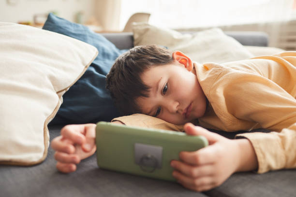 bored little boy using smartphone - pereza fotografías e imágenes de stock