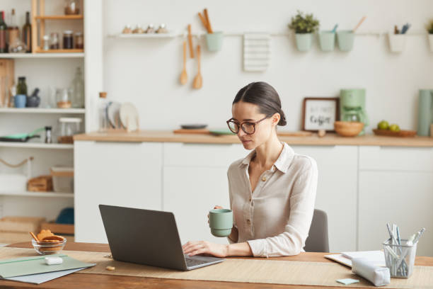 istock Elegant Young Woman Using Laptop in Kitchen 1250438591