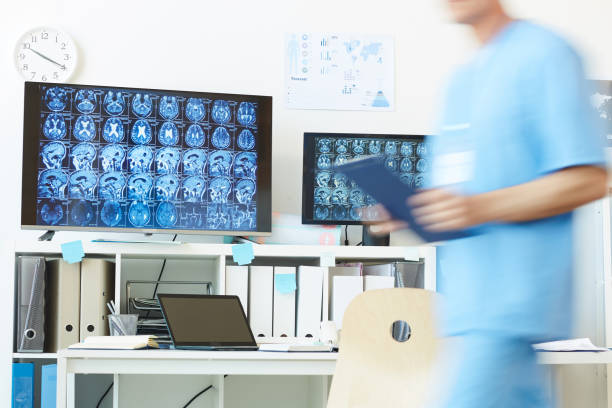 Brain Computer Tomography Images Background image of modern computer equipment with CT brain scans on screens at work station and blurred shape of unrecognizable medic walking in foreground, copy space neurodegenerative disease stock pictures, royalty-free photos & images