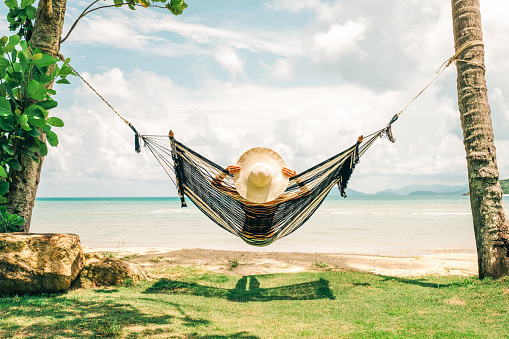 Summer vacations concept. Happy woman in black bikini relaxing in hammock on tropical beach