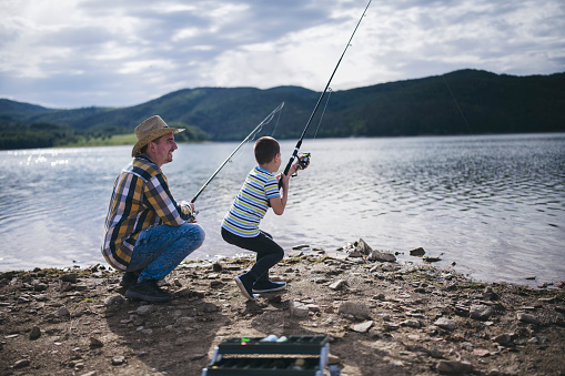 Dad shows his son how to hold the spinning and spin the reel. Fishing training on a pond or river. Caring parent concept. Father and son fishing.