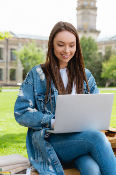istock cheerful student sitting on bench and using laptop near books, online study concept 1250457411