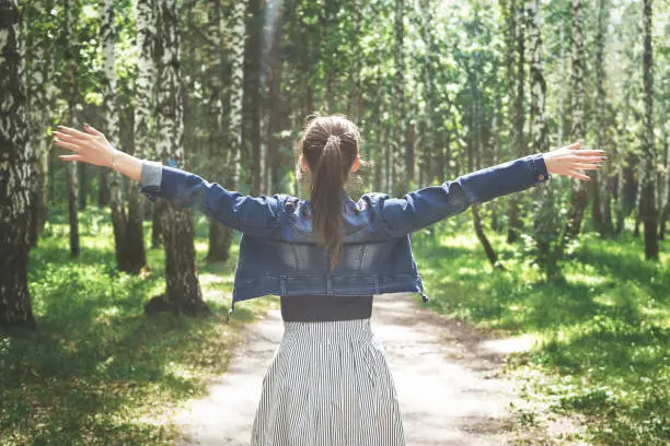 Young woman in denim and dress, standing in the forest and spread her hands wide. Relaxation concepts