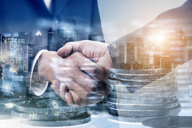 Double exposure of businessman handshake with stack of coins and city night background, money or revenue of saving and invest concept stock photo