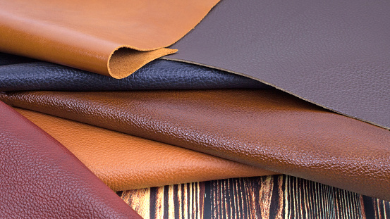 Different colors natural leather textures samples on dark wooden background