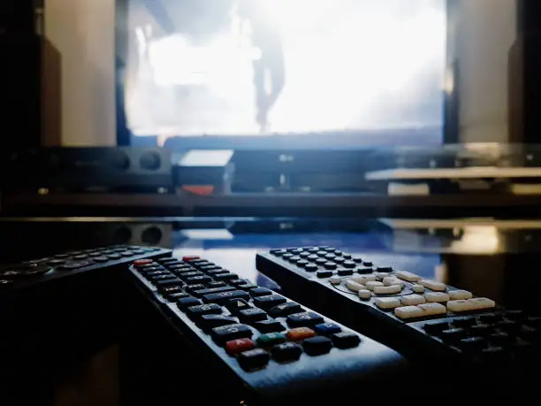 Photo of Collection of remote controls in front of a bright TV set