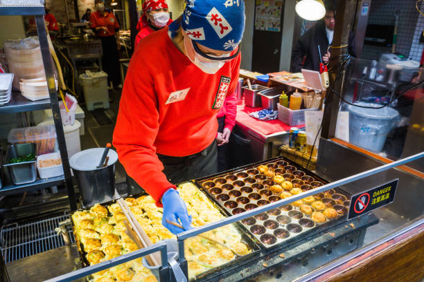 Osaka chef cooking takoyaki street food market stall Dotonbori Japan Chef preparing traditional octopus takoyaki at a street food stall in the popular Dotonbori district of central Osaka, Japan. cooking takoyaki is a ball shaped japanese snack stock pictures, royalty-free photos & images