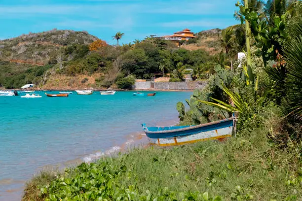 Photo of Small wooden bard, standing in the vegetation of Ferradura beach, with blue sea and houses in the background, Buzios, Rio de Janiero, Brazil
