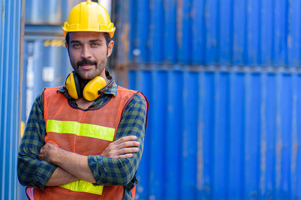 istock Young confident man engineer using digital tablet and wearing yellow safety helmet and check for control loading containers box from Cargo freight ship for import and export, transport. 1250470992