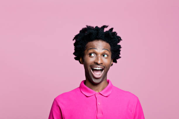 headshot de jovem surpreso vestindo camisa polo rosa - polo shirt african ethnicity men african descent - fotografias e filmes do acervo