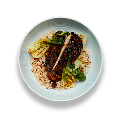 A delicious bowl of Jerk chicken, rice and vegetables, in a light blue bowl isolated on a white background