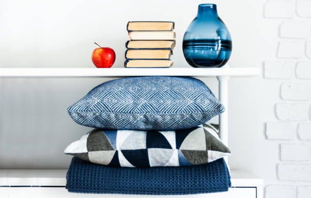 istock Cozy home interior decor: pillow, plaid, blue vase, stack of books, red apple on a white shelf in the room. The quarantine concept of stay home, distance home education background 1250480761
