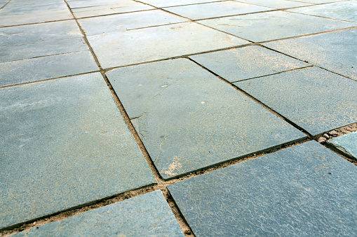 Green slate patio before re-grouting with gaps between slate slabs as weathering has damaged the mortar.