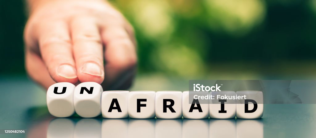 Hand turns dice and changes the word "afraid" to "unafraid". Adventure Stock Photo