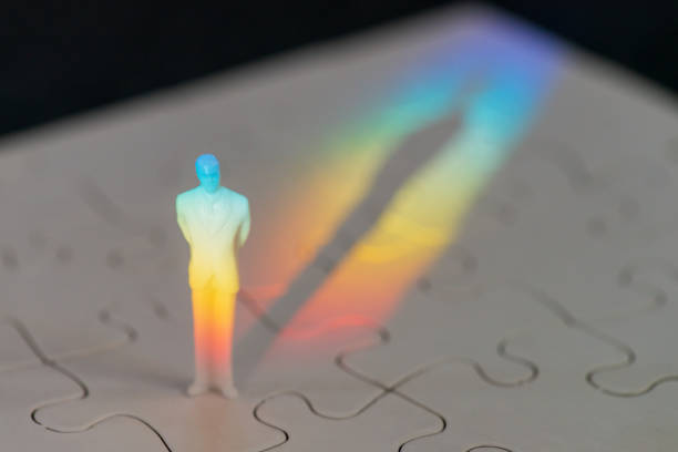 Puzzled man Close-up of a miniature figurine of a man standing on a blank jigsaw puzzle, illuminated by the colours of light refracted through a prism. legacy concept stock pictures, royalty-free photos & images