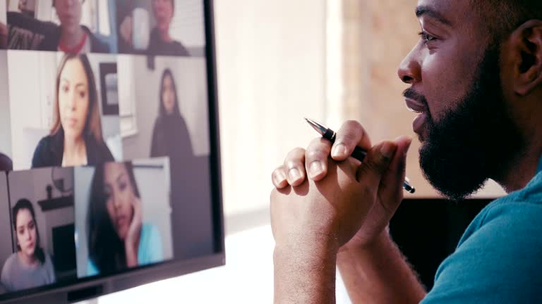 A confident mid adult businessman shakes his head in understanding or agreement during a virtual staff meeting via video conference. The colleagues are meeting virtually during the COVID-19 quarantine.