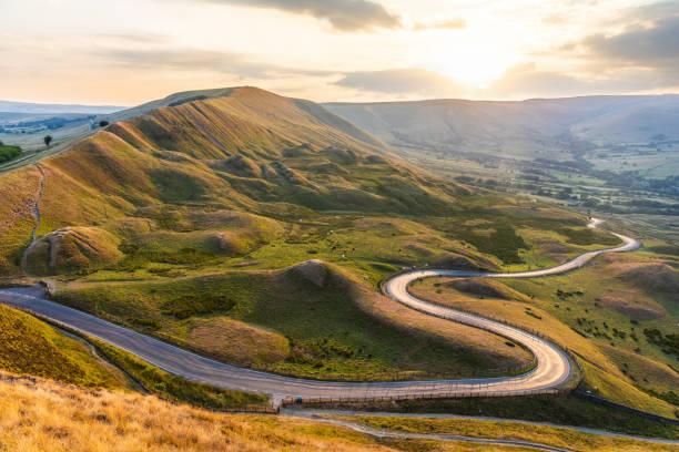Beautiful winding road and hills at sunset in the Peak District - Landscape view with golden light in the UK - Nature and travel concepts, background ready image Beautiful winding road and hills at sunset in the Peak District - Landscape view with golden light in the UK - Nature and travel concepts, background ready image peak district national park photos stock pictures, royalty-free photos & images