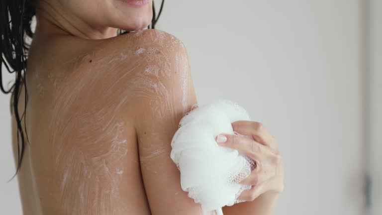 Young 20s woman using loofah bath puff in shower.