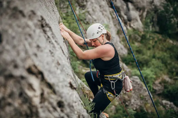 One young woman, free climber, with a rope climbing on the rock mountain in nature.