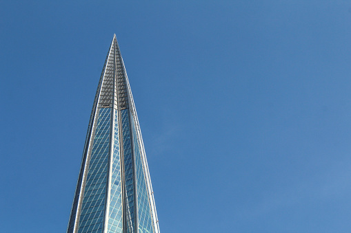 The spire of the office building is made of glass against the blue sky.