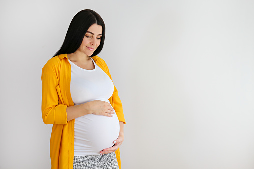 Portrait shot of young beautiful woman on third trimester of pregnancy. Close up of pregnant female with arms on her round belly. Expecting a child concept. Background, copy space.