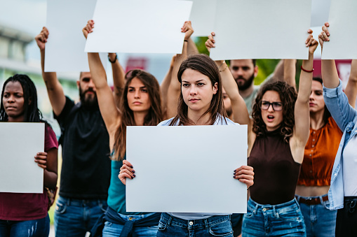 Young people protesting at the street with blank, white placards and posters.