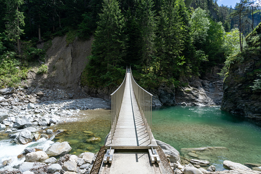 A modern wooden suspension bridge across the Rhine River in the heart of the Viamala Gorge in the Swiss Alps