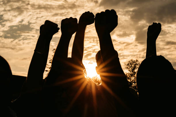 silueta de puños levantados al atardecer - shaking fist fotografías e imágenes de stock