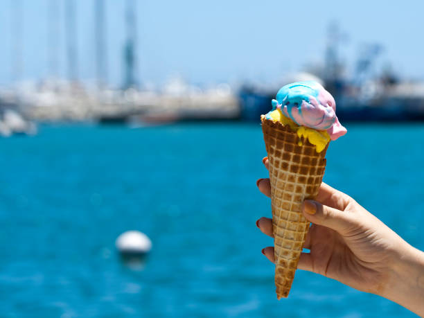istock Ice cream cone in hand in front of blurred blue sea 1250510526