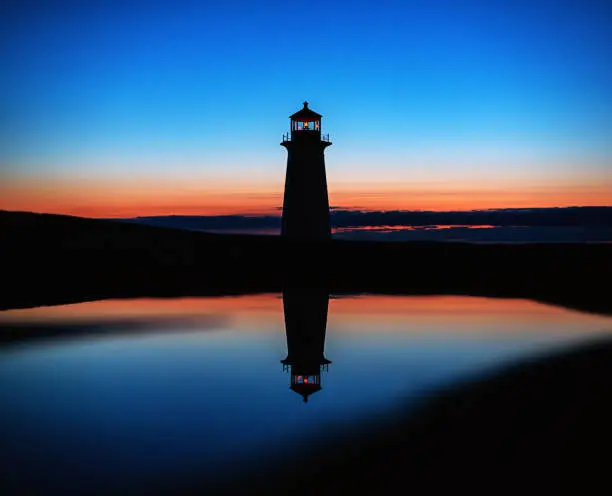 Peggy's Cove lighthouse is reflected in a still puddle in deep twilight.