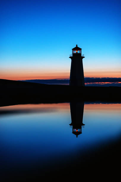 Peggy's Cove lighthouse is reflected in a still puddle in deep twilight.