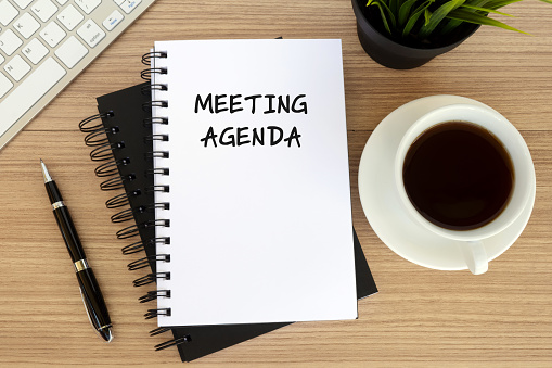 Meeting agenda text on note pad with cup of coffee