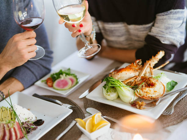 coppia che gusta frutti di mare gourmet con bicchieri di vino rosso e bianco - gourmet food lobster seafood foto e immagini stock