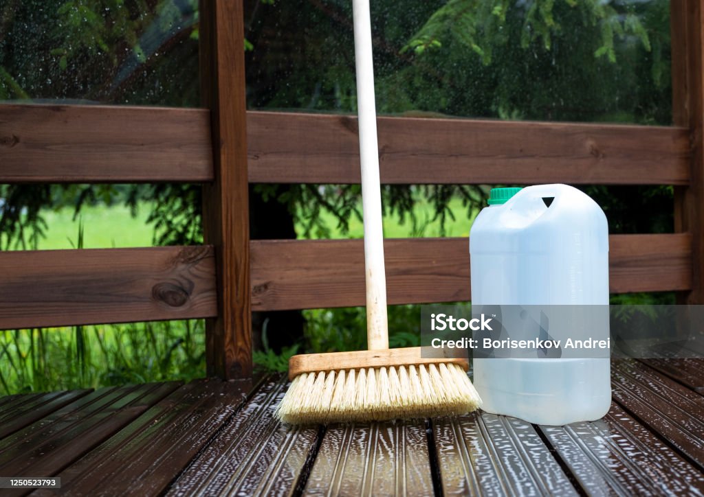 Brush, plastic canister with chemical solution and soap solution on the wooden planks of the terrace. Brush, plastic canister with chemical solution and soap solution on the wooden planks of the terrace. Cleaning and maintenance of cleanliness in the country house. View from above Cleaning Stock Photo