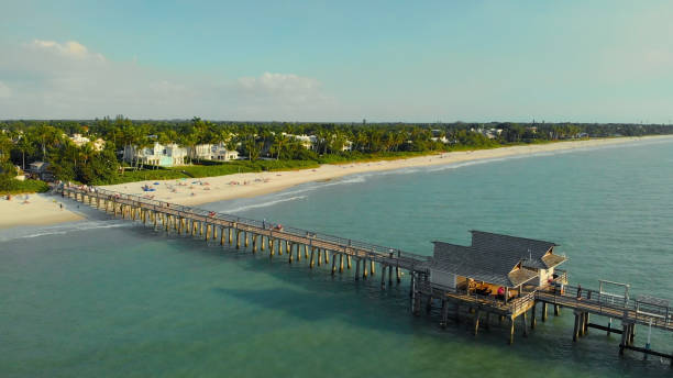Naples Beach and Fishing Pier at Sunset, Florida Pier in Naples by Aerial Drone. Drone flies around a fishing pier in Naples, Florida USA. Coast and the beach near the pier leaving into the ocean. Naples Beach Pier. naples beach stock pictures, royalty-free photos & images