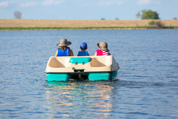 Rear View of Three Children In Paddle Boat on Small Lake Rear view of three children in a paddle boat on a small lake. Two girls are on either side of their little brother, who is sitting in the middle. paddleboat stock pictures, royalty-free photos & images