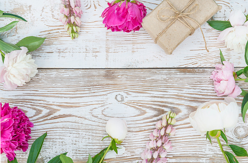 Floral background with peonies and handmade gift box. White paint wooden background. Space for text, flat lay