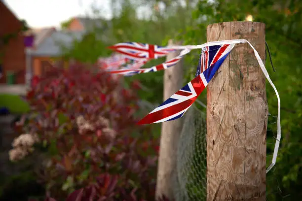 Union Jack flag bunting attached to wooden post/fence blowing in the wind with soft bokeh background.