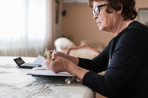 Worried older woman sitting at a table and calculating her expenses