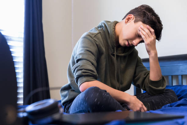istock Depressed teen sits on bed with head in hand 1250539084
